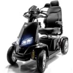 A black, four-wheeled mobility scooter with a high-back padded seat, armrests, and control handlebars. It features headlights and is designed for outdoor use, providing comfortable transportation for individuals with mobility challenges.