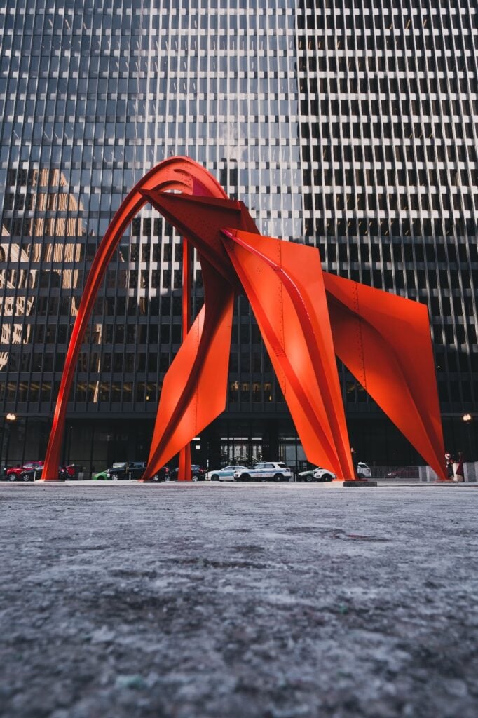 A vibrant red 'Flamingo' sculpture by Alexander Calder in Chicago's Federal Plaza, contrasting with the surrounding high-rise buildings.