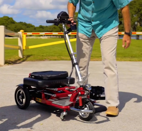 Man folding a folding scooter outdoors.